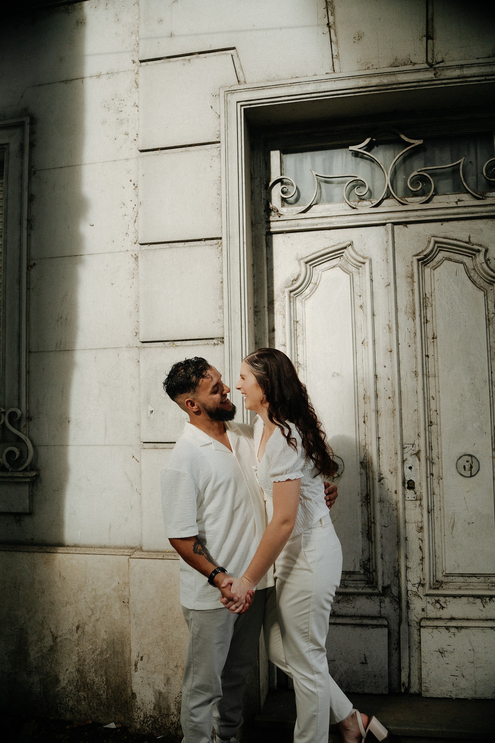 Pareja con outfits blanco y crema frente a puerta vintage - ejemplo de paleta editorial para pre-boda - Lucas Todaro Buenos Aires